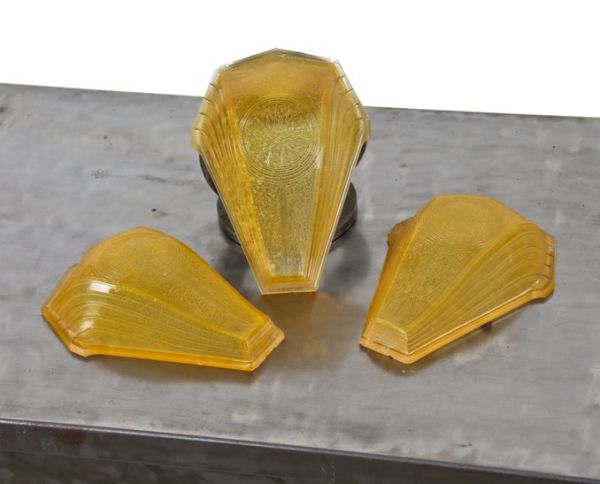 group of three matching streamlined style american art deco amber-colored ornamental pressed glass slip shades with highly stylized sunburst motif