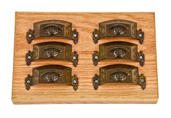 six matching original 19th century mounted ornamental cast iron "all-seeing eye" drawer or bin handles with oak plaque