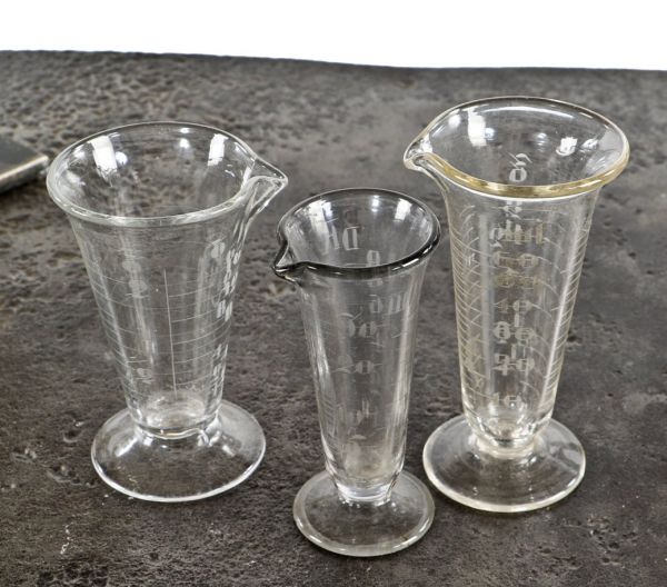 three nearly identical early 20th century antique american apothecary drugstore acid or wheel-cut etched clear glass conical-shaped measures with pedestal bases