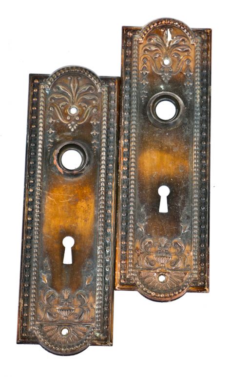 set of two matching original and well-maintained early 20th century oxidized copper-plated finish stamped metal "como" pattern doorknob backplates