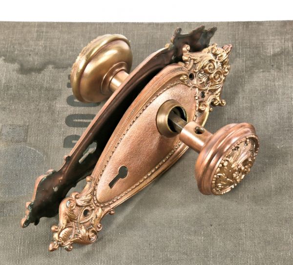 one of several matching brass-plated cast bronze interior residential late victorian era passage door locksets comprised of decorative doorknobs and uniquely shaped backplates 