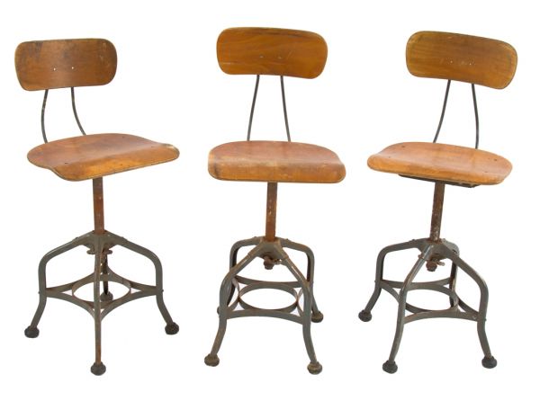 group of three matching fully adjustable "uhl art steel" factory machine shop stools with wood saddle seats, contoured backrests, and intact black rubber feet