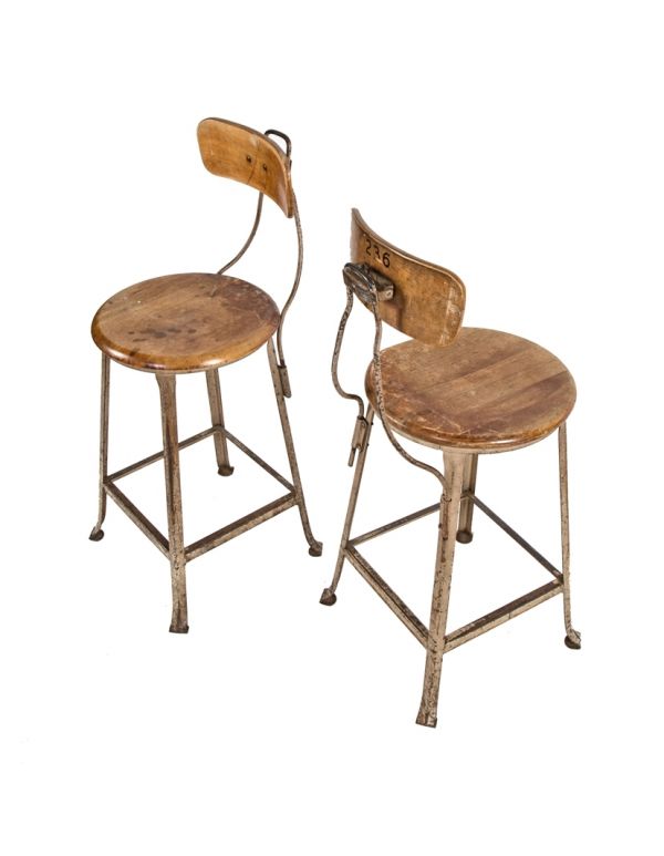 pair of matching weathered and worn numbered stationary salvaged chicago tool and die factory machinist stools with original maple wood seats and contoured backrests 