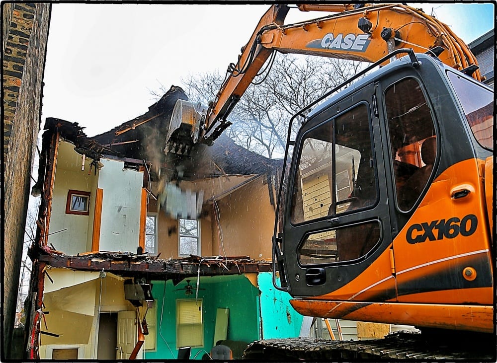 the mid-sized excavator quickly reduces the wood framed dwelling to rubble.